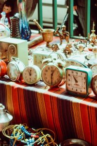 A collection of old-fashioned alarm clocks displayed on a colorful table at an outdoor flea market.